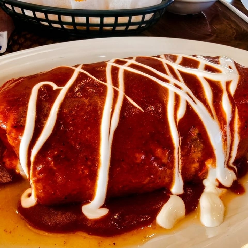 A large burrito covered in red sauce and drizzled with white sour cream on a white plate.