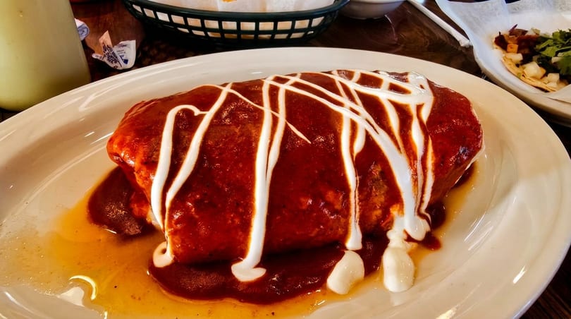 A large burrito covered in red sauce and drizzled with white sour cream on a white plate.