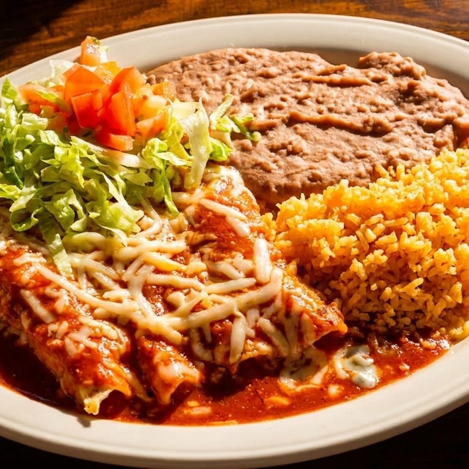 A plate of enchiladas with red sauce, melted cheese, lettuce, tomatoes, refried beans, and rice.