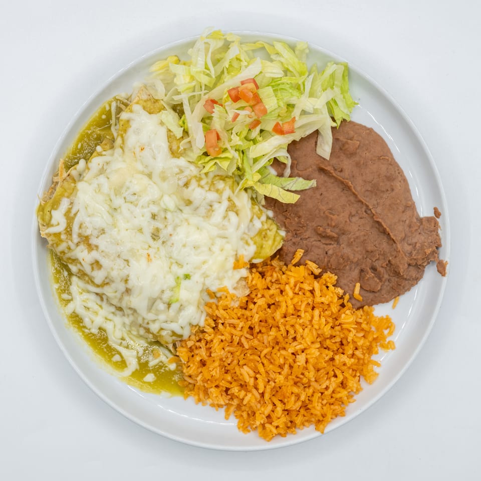 A plate of enchiladas with green sauce, melted cheese, shredded lettuce, diced tomatoes, refried beans, and orange rice.