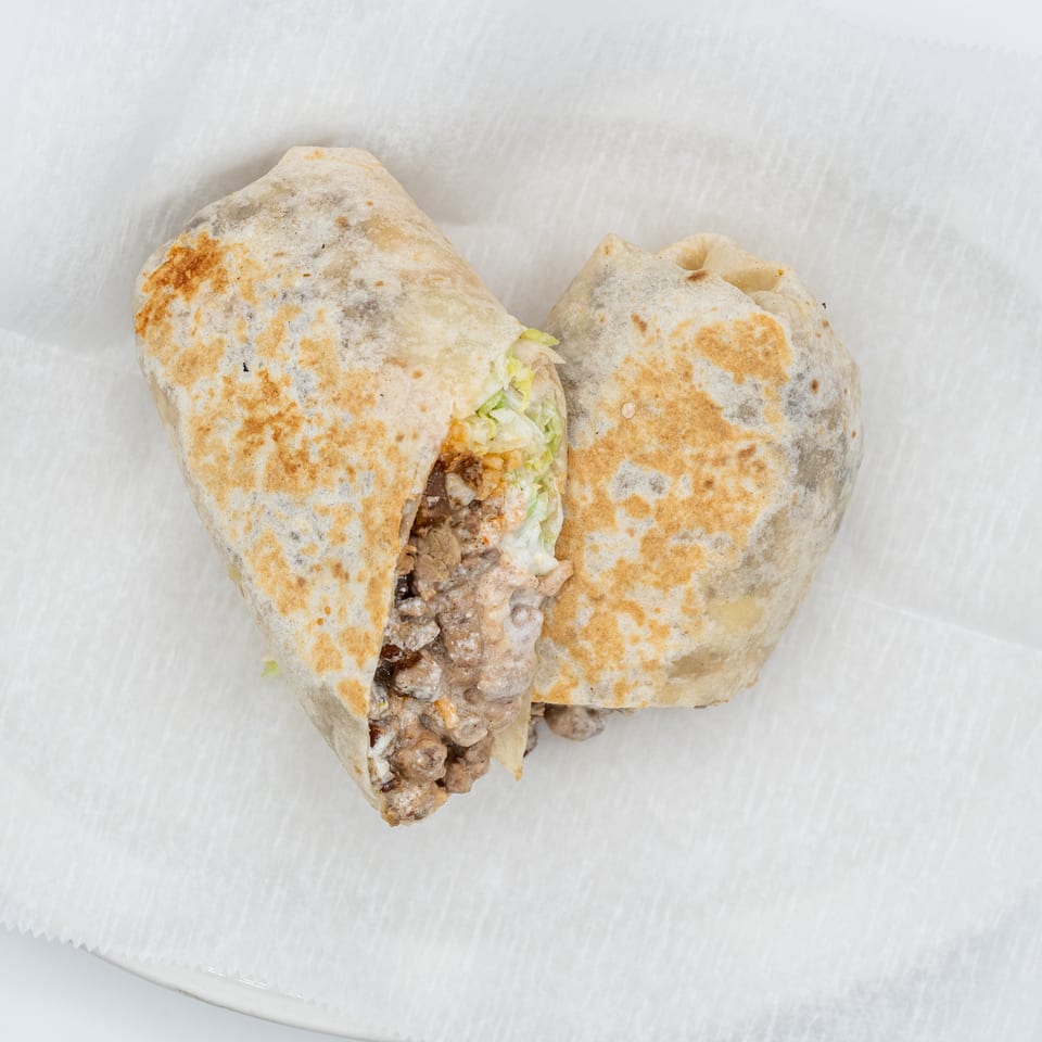 Two large burritos, one cut open revealing meat, cheese, and lettuce, on white parchment paper.