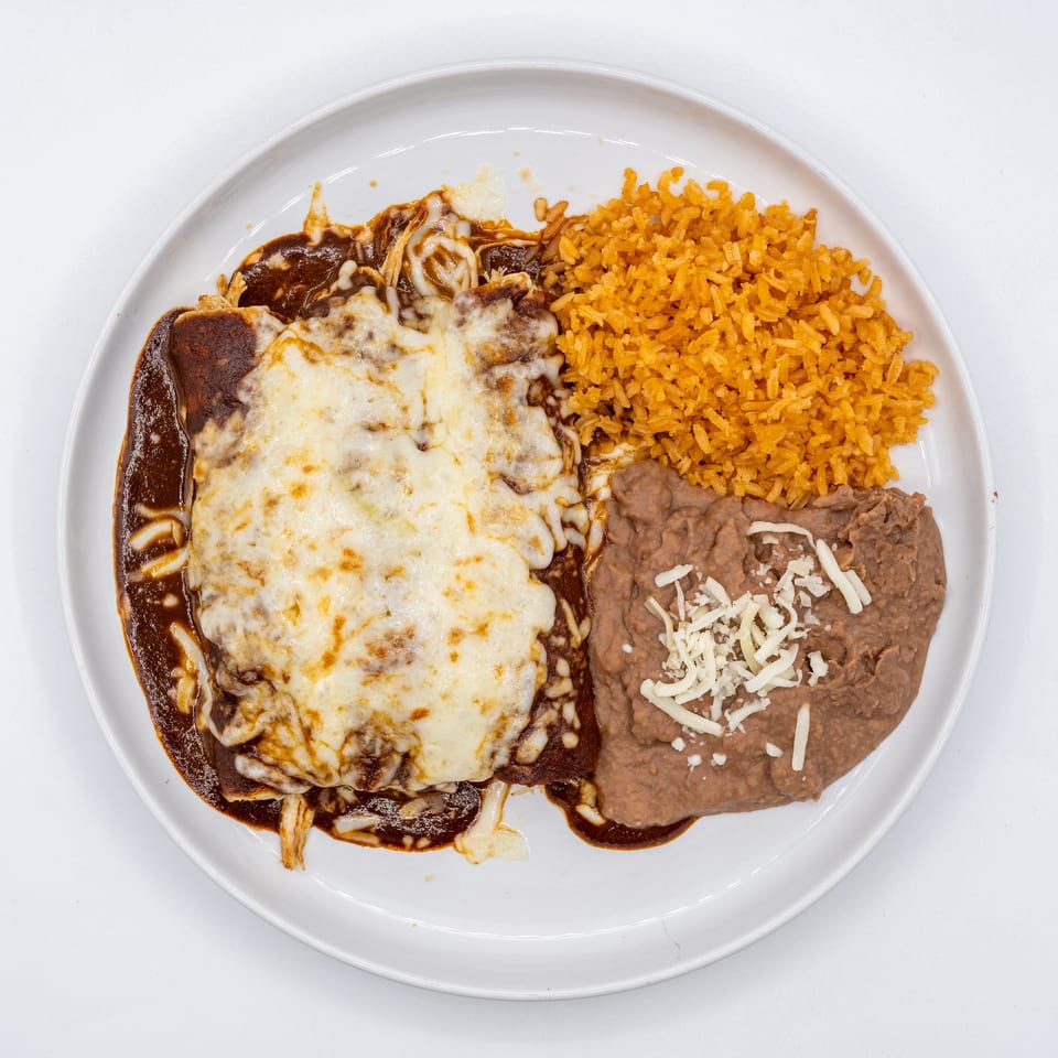 Enchiladas with mole sauce and melted cheese, served with orange rice and refried beans.