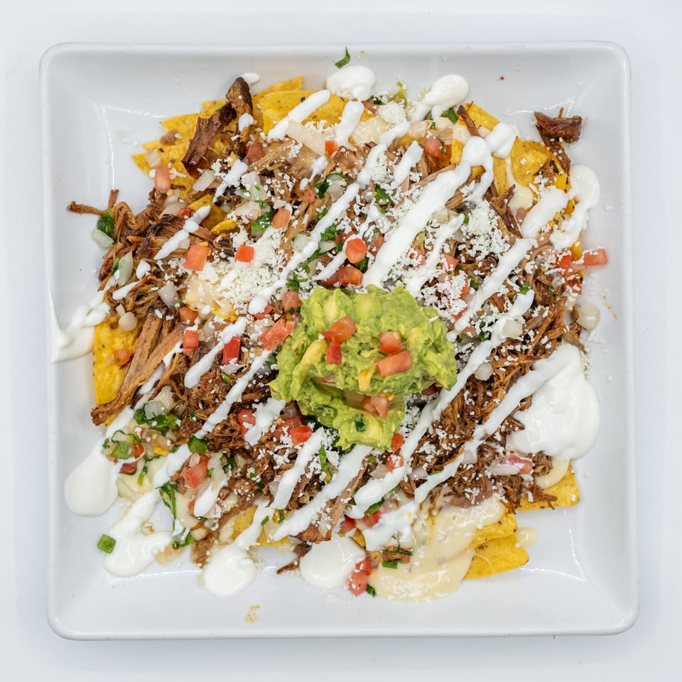 Loaded nachos with shredded meat, guacamole, sour cream, cheese, and pico de gallo.