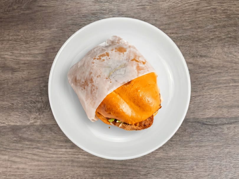 Top-down view of a sandwich wrapped in paper on a white plate, on a wooden table.